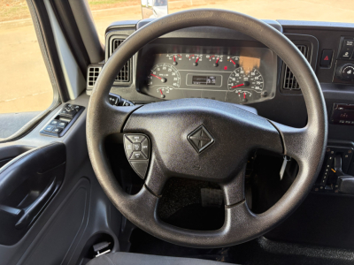 Truck cab interior showing steering wheel and dashboard gauges from International MV607 with steering wheel center diamond logo and instrument cluster.