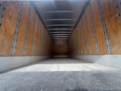 Truck trailer empty cargo area with wooden side walls and metal rails, interior seen from back doorway, long rectangular box truck trailer