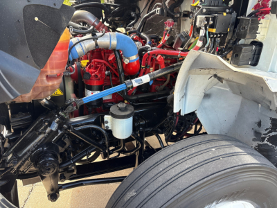 Truck engine bay with blue intercooler hose, red engine components, coolant reservoir, and suspension visible in a 2020 International MV607.