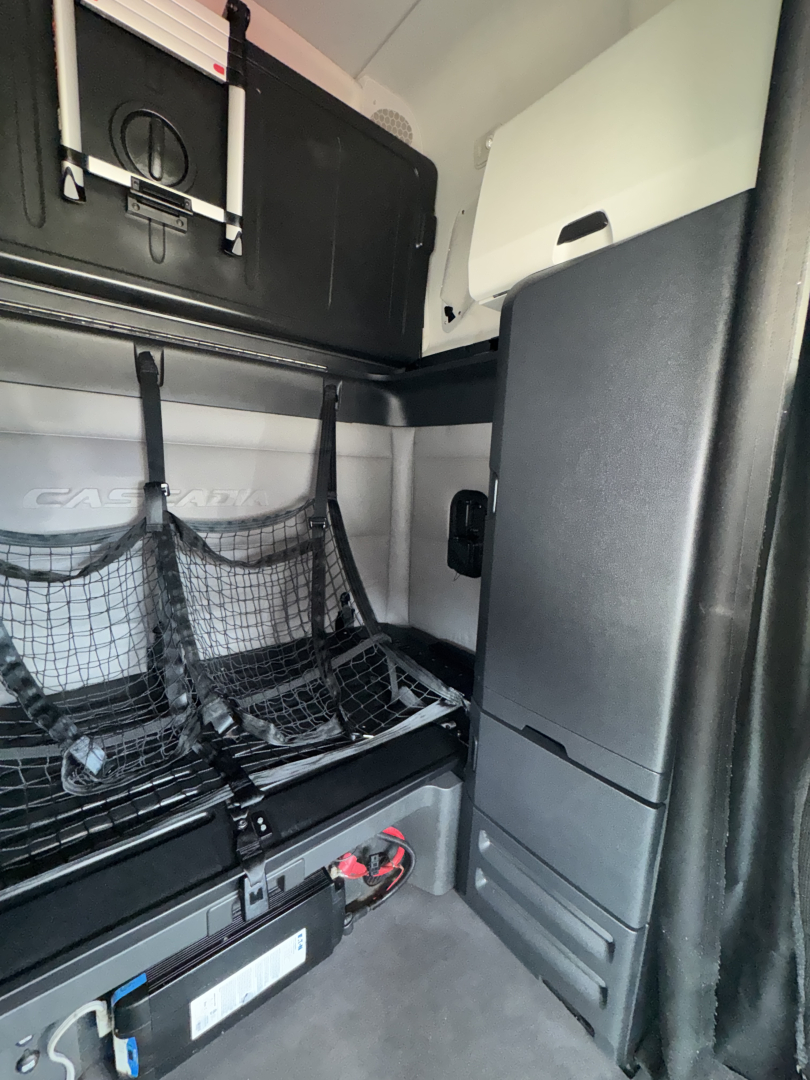 Freightliner Cascadia cab interior showing sleeper area with netted storage and vertical cabinet.