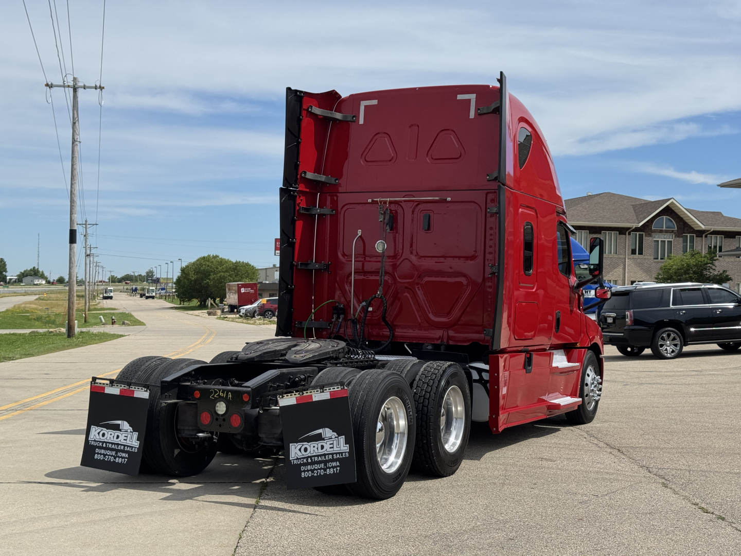 Freightliner Cascadia 126 tractor rear view showing dual rear axles with mud flaps and red sleeper cab; visible text on mud flaps: Kordell Trucks; street in background.
