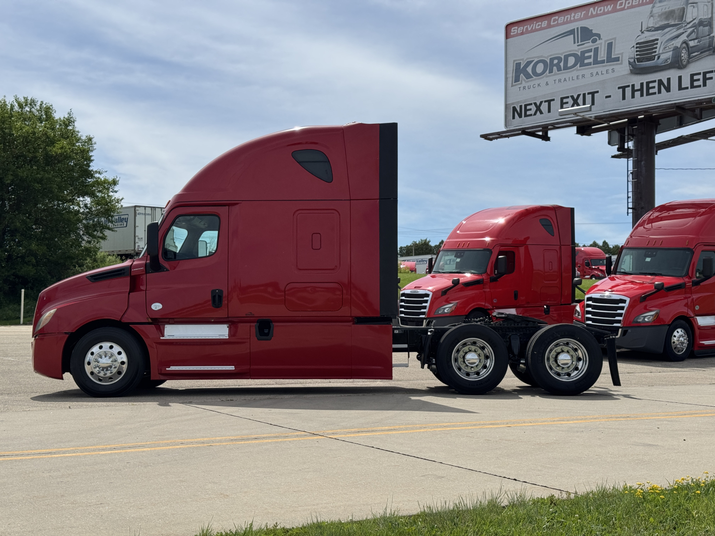 2019 Freightliner Cascadia 126 tractor truck side view showing sleeper cab and tandem rear axles in a dealership lot.