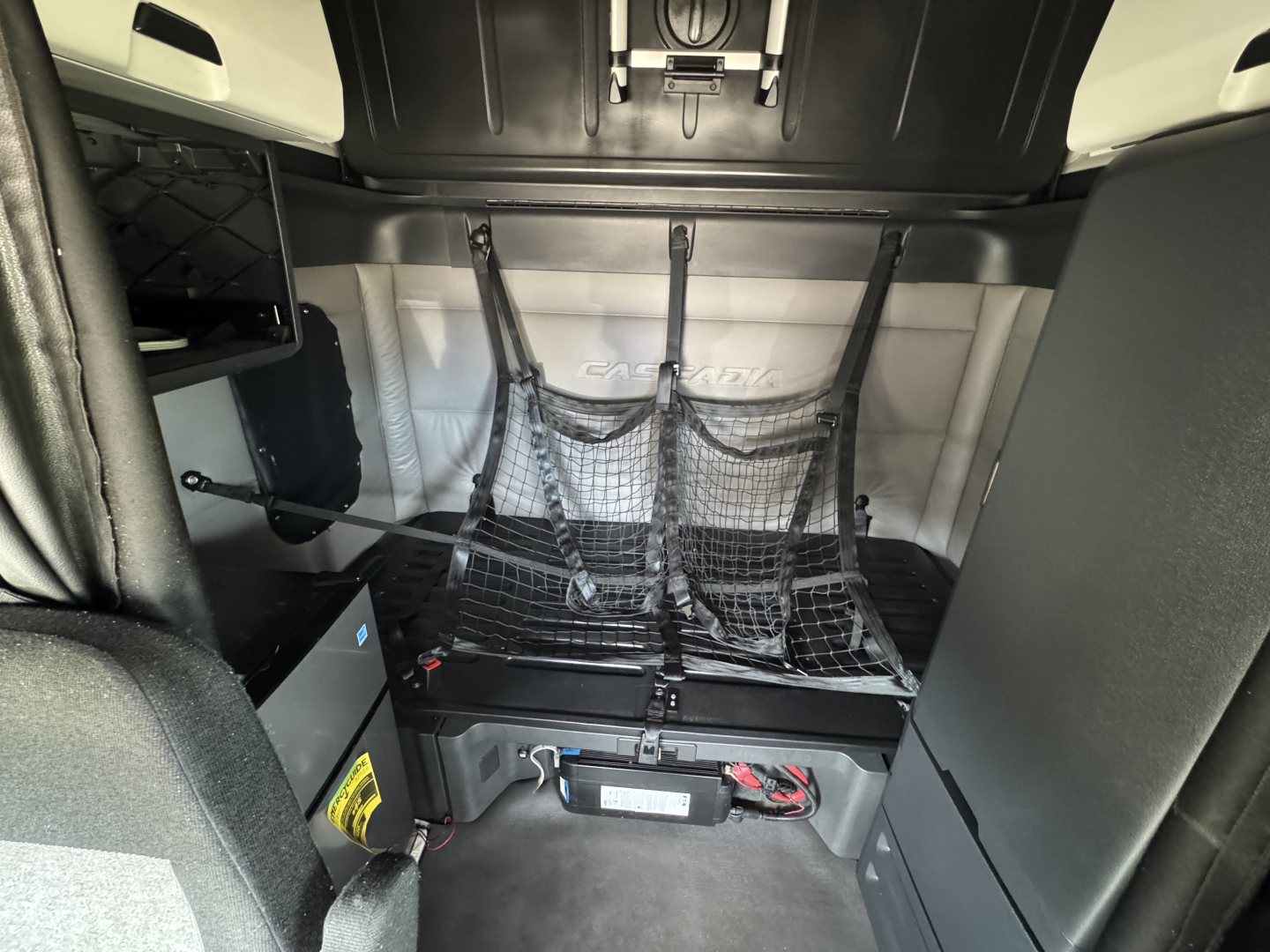 Freightliner Cascadia 126 sleeper cab interior rear bunk area with storage net and cargo strap system visible.