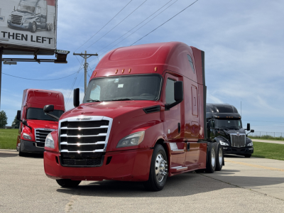 Freightliner Cascadia 126 truck in red in a dealership lot with two other trucks in background.