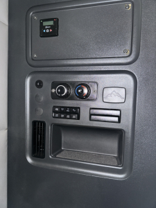 Dashboard panel inside a Freightliner Cascadia cab showing a small screen, climate controls, and storage compartment; no legible VIN or stock numbers visible on this panel.