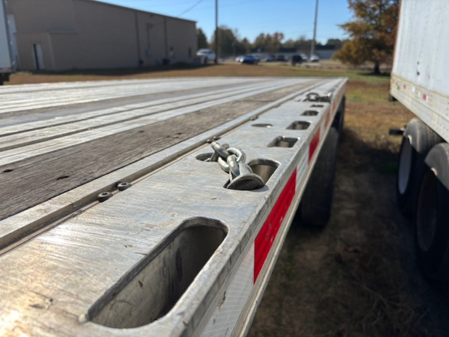 Flatbed expandable trailer edge with recessed tie-down rings and red reflective markers; aluminum decking and wheel well visible; part of Fontaine Infinity trailer.