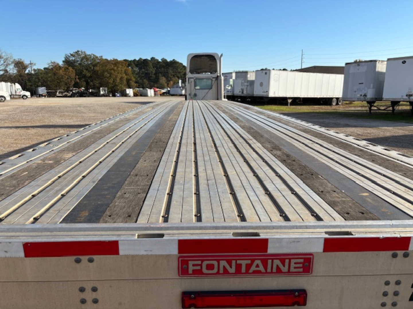 Flatbed trailer deck with extended metal planks and Fontaine logo on rear bumper.