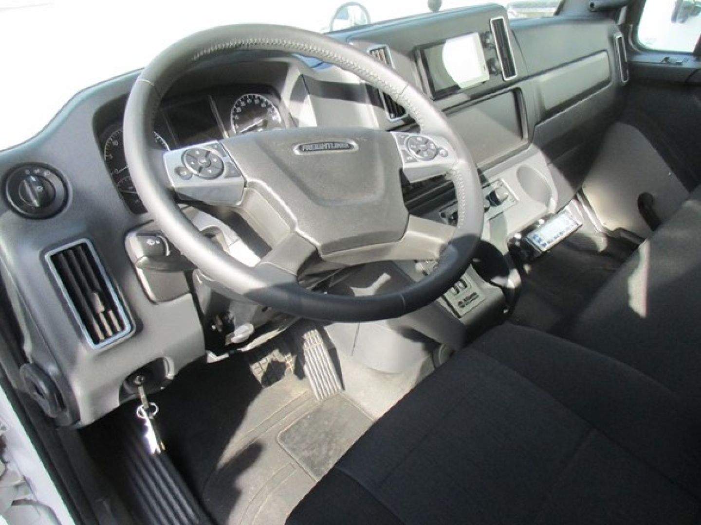 Freightliner M2 106 Plus cockpit showing steering wheel and dashboard with controls.