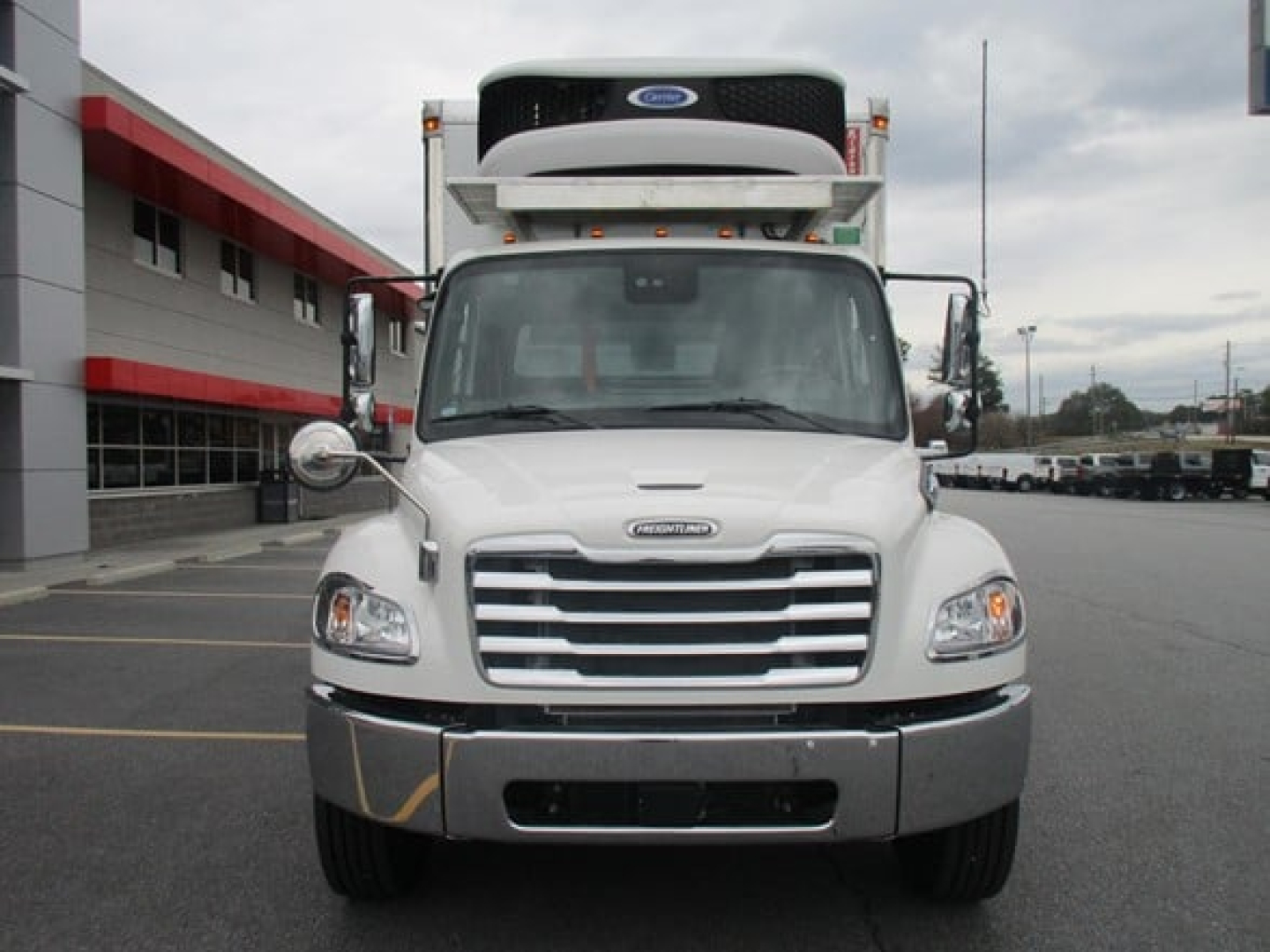 Front view of a white Freightliner M2 106 Plus refrigerated truck with a cooling unit on the roof, chrome grille, and large bumper.