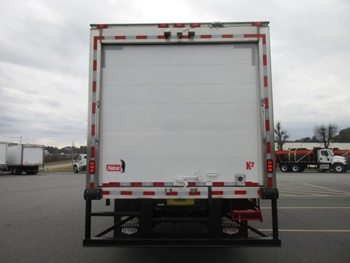 Freightliner M2 106 Plus refrigerated truck rear view showing liftgate and rear doors, white cargo area with red/white reflective tape.