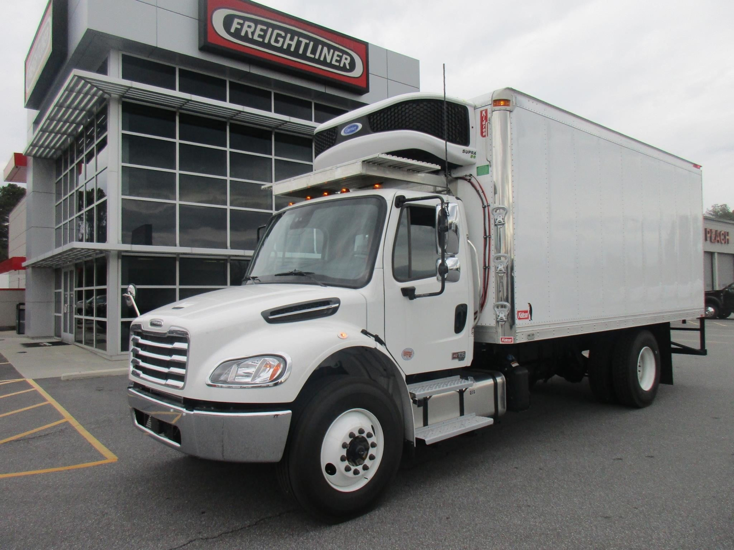 Freightliner M2 106 Plus refrigerated truck in front of dealership, white cab and box, VIN 1FVACXFE5THWR3410 visible, stock number 327454.