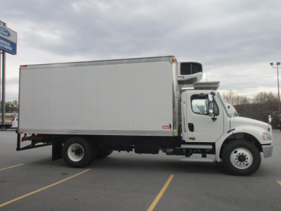 Freightliner M2 106 Plus refrigerated truck in a parking lot, side view. Side of cab shows wheel wells and cargo box; no legible text visible on decals.