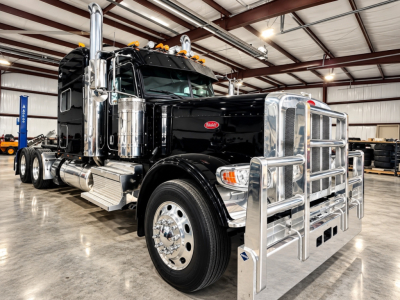 Peterbilt 389 conventional sleeper truck in a showroom featuring a large chrome grille guard and polished chrome exhaust stacks.