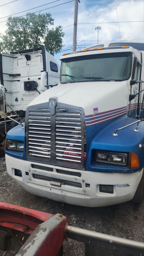 Kenworth T600 truck in a yard, front view showing chrome grille, dual headlights, blue and white paint with red stripe, hood ornament, clearance lights on roof.