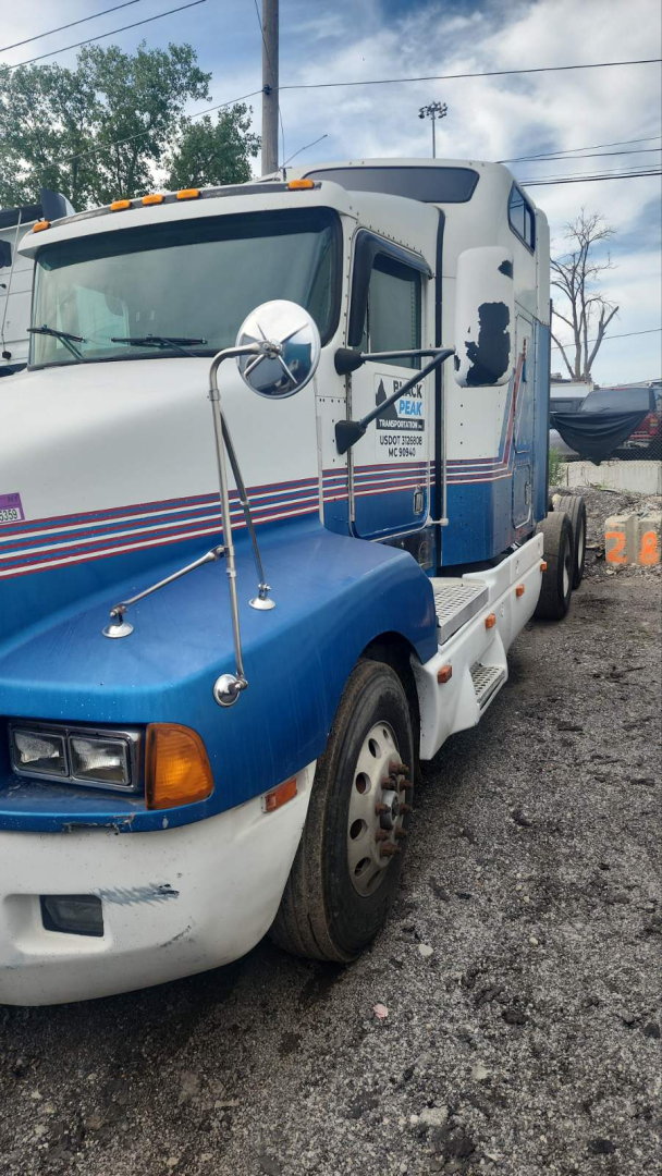 Kenworth T600 tractor showing side view with blue and white paint, cab mirrors, and warning lights on top; VIN plate and model markings faint on door.