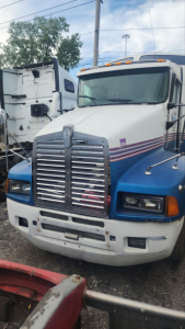 Kenworth T600 truck in a yard, front view showing chrome grille, dual headlights, blue and white paint with red stripe, hood ornament, clearance lights on roof.