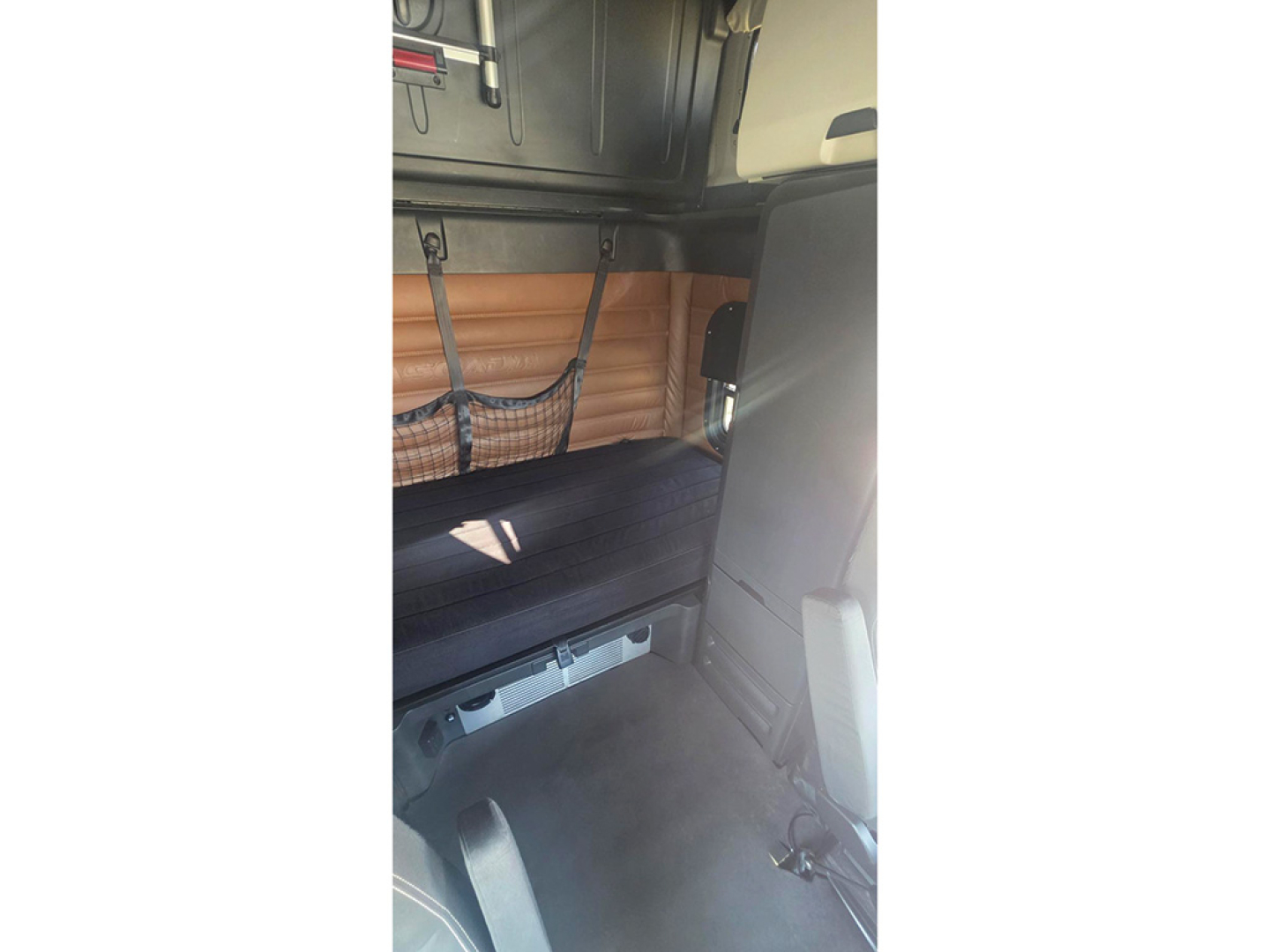 Truck cab interior showing brown padded sleeper wall, black mattress, and storage netting with metal hooks.