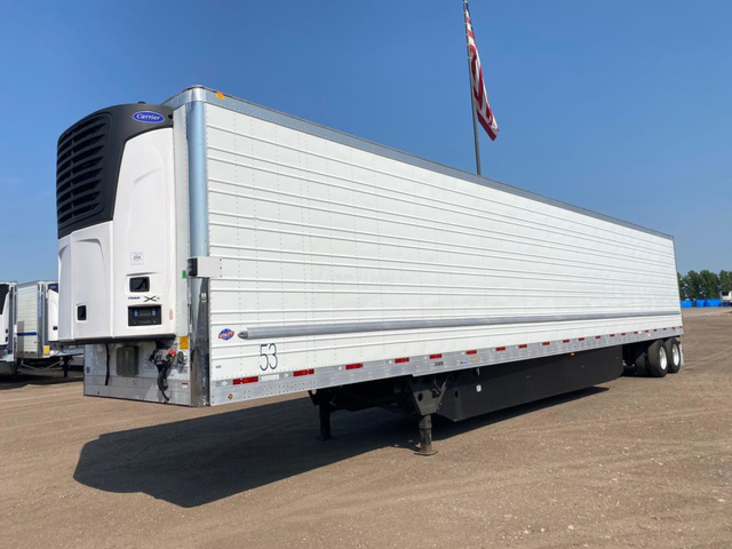 Utility reefer trailer with a white refrigerated box and black refrigeration unit at the front. Side text shows no visible branding; trailer stands on landing gear with a hitch and a triple-axle rear.