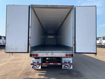 Refrigerated trailer interior showing empty cargo space with open rear doors in a yard.
