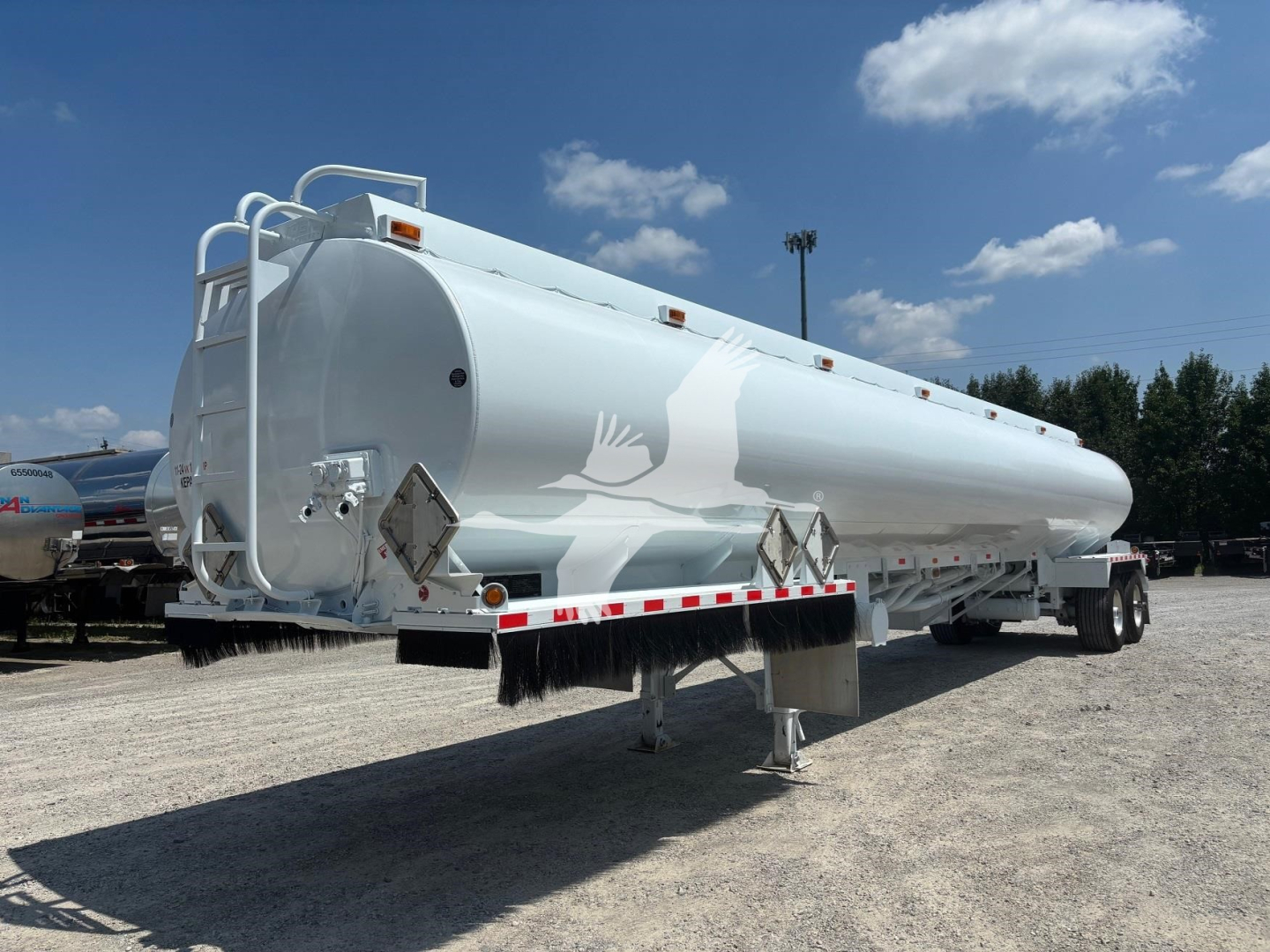 Flat side view of a white Heil 9200 tanker trailer with ladder and protective railing, parked on gravel.