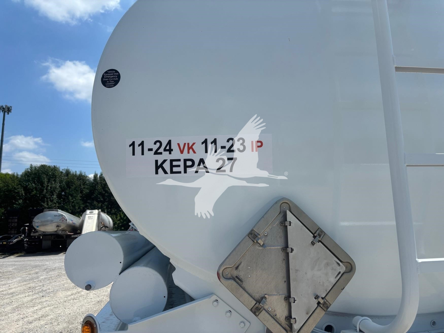Rear of a Heil 9200 trailer showing a triangular access door and painted markings including '11-24 VK 11-23 IP' and a white bird silhouette logo near the back end.