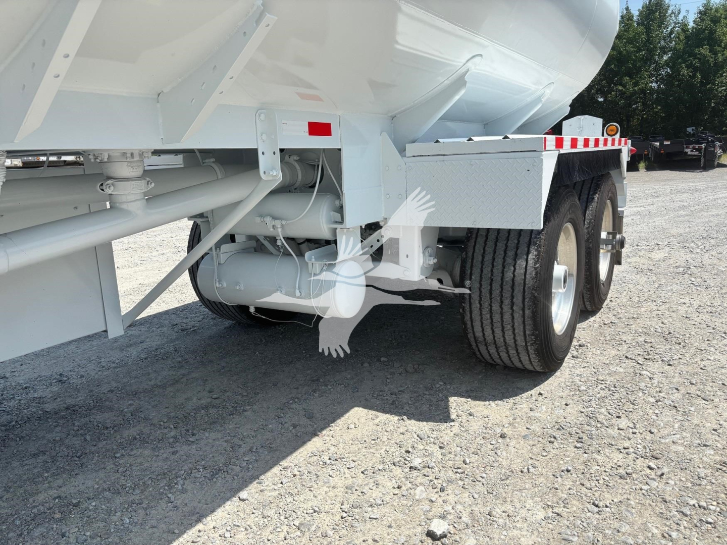 Trailer undercarriage showing dual rear axles with tires and undercarriage components including a cylindrical tank and support frame; no legible text visible on components.