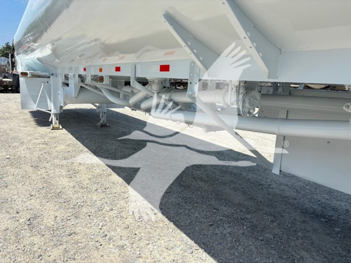 Trailer undercarriage showing frame, suspension, and support legs with reflective tape; aluminum trailer with white paint and gravel ground.