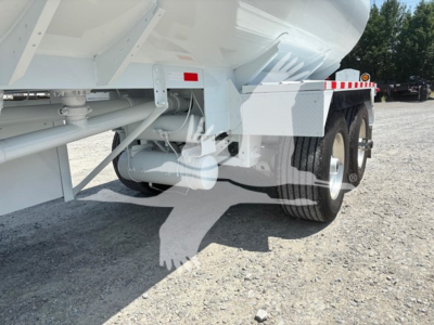 Trailer undercarriage showing dual rear wheels and axles of a tank trailer, welded frame, suspension components, and underside pump area.
