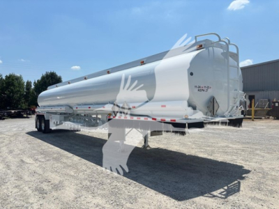 Truck trailer shown in a yard; white Heil DOT406 fuel trailer with rounded cylindrical tank, dual tandem axles, rear ladder, and safety stripes.