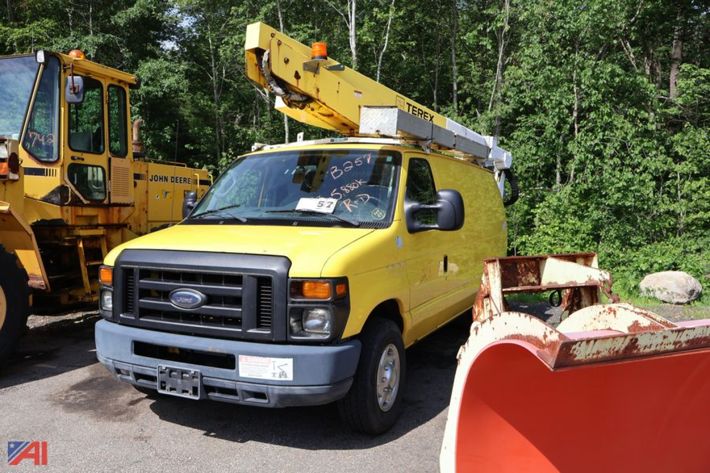 Ford E-350 bucket truck in yellow with crane elevated, front view showing truck cab and bucket arm, with additional equipment in background.