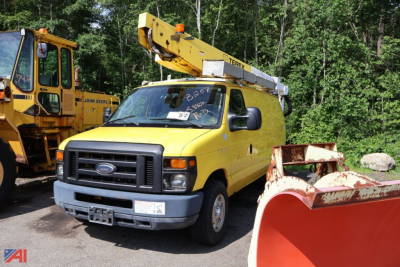 Ford E-350 bucket truck in yellow with crane elevated, front view showing truck cab and bucket arm, with additional equipment in background.