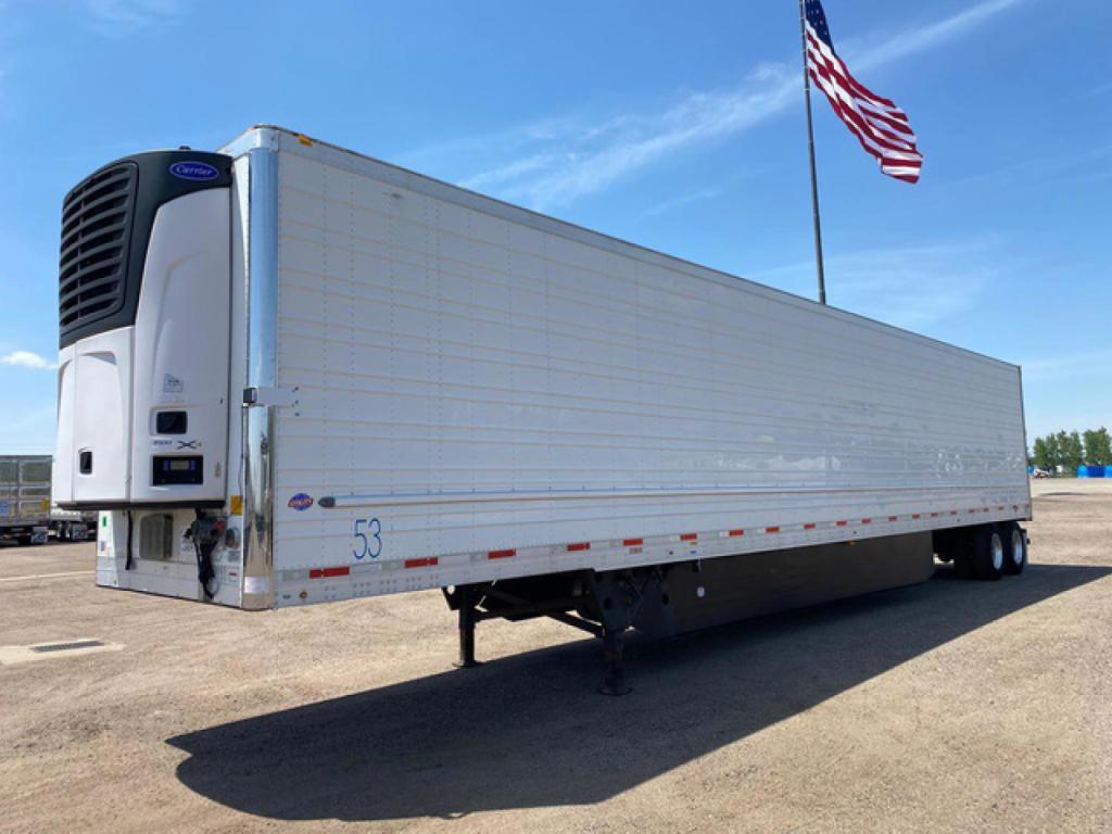 Trailer side view showing a white refrigerated utility trailer with a blue Ford refrigeration unit at the front and an American flag in the background.