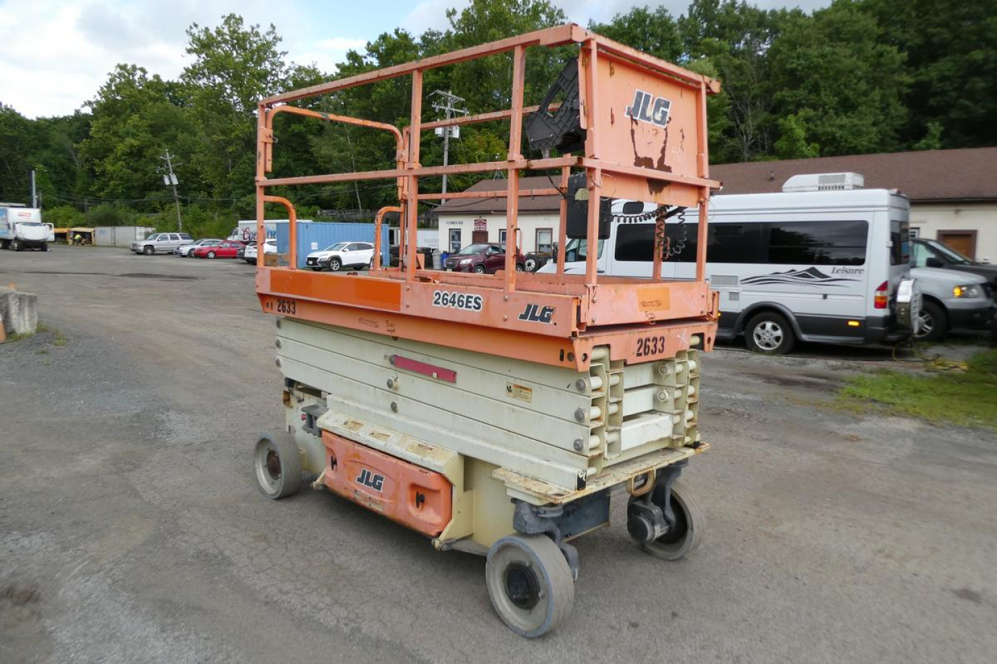 JLG 2646ES scissor lift in a yard, orange guardrails, white lower sections, with JLG branding and model number visible on side.