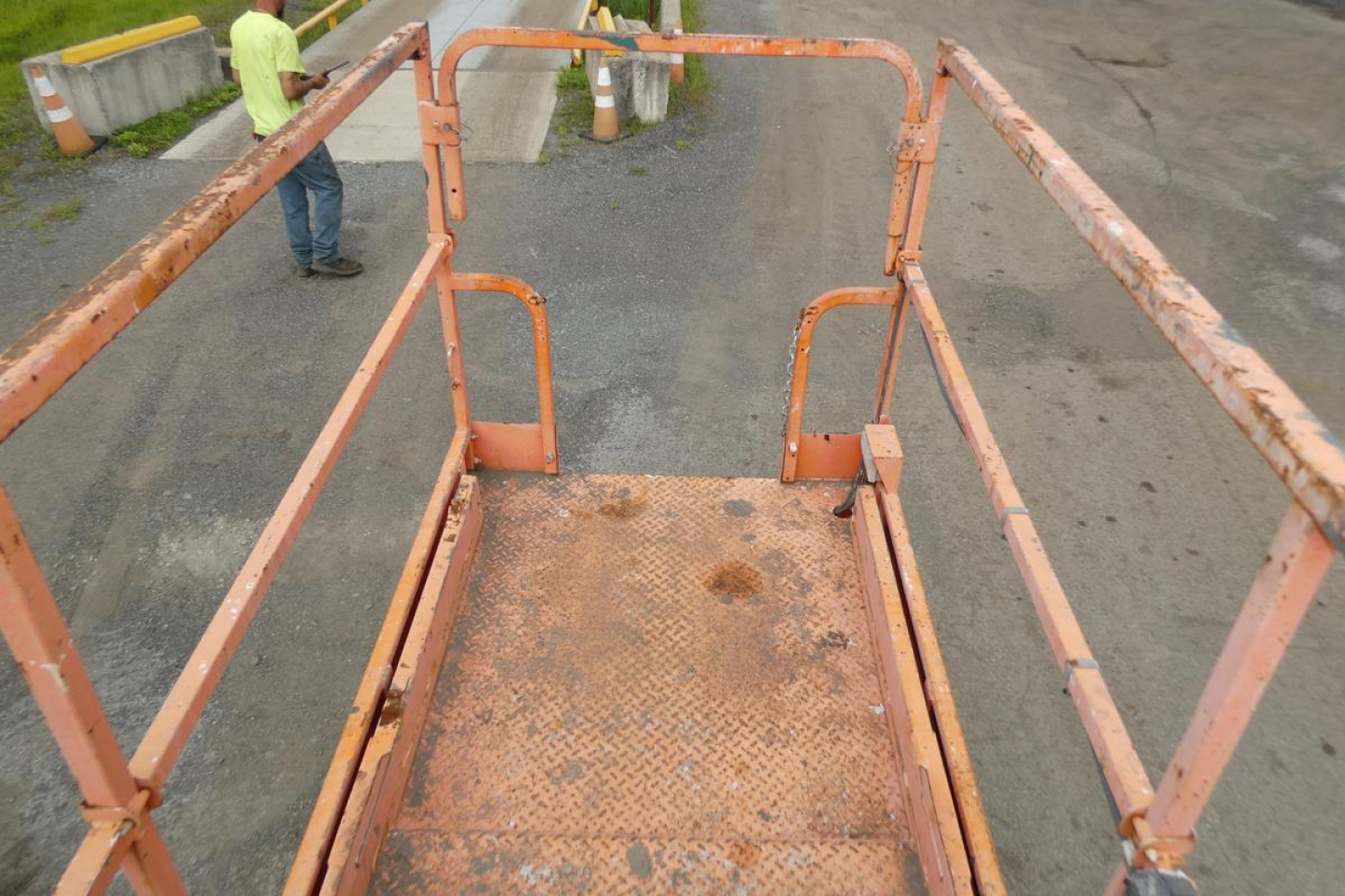 Scissor lift platform with orange railing and rusted deck showing wear from use.