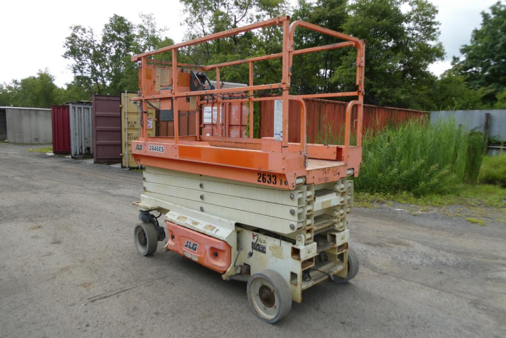 JLG 2646ES scissor lift in-use condition showing orange guardrails and beige base with serial/asset stickers visible.