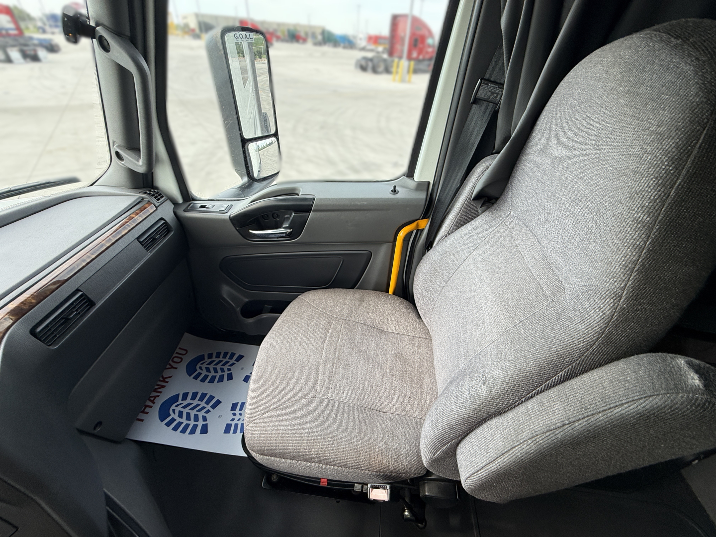 Truck cabin interior of a 2022 International LT625 with gray fabric seat, dashboard, and open door; exterior view shows side mirror and yard.