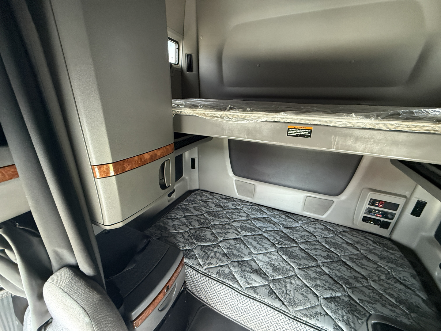 Truck sleeper bunk area in a 2022 International LT625 showing a quilted mattress, storage compartments, and side panel with controls.