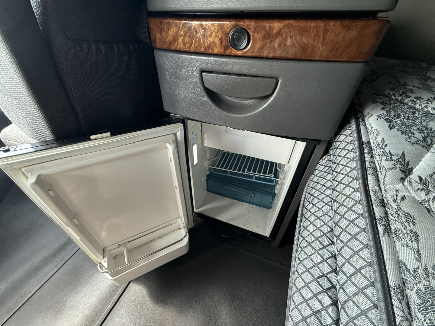 Mini fridge in truck sleeper cab with open door and interior shelves visible.