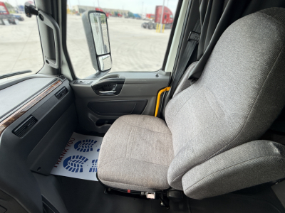 Truck cabin interior of a 2022 International LT625 with gray fabric seat, dashboard, and open door; exterior view shows side mirror and yard.