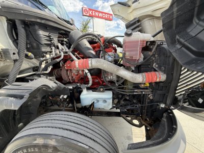 Engine bay of a 2022 International LT625 truck showing red diesel engine, radiator hoses, coolant reservoir, and front suspension components.