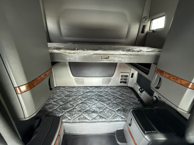 Interior of a 2022 International LT625 sleeper cab showing bunk bed area, storage compartments, and quilted cab floor; compact control panel and wood trim accents.
