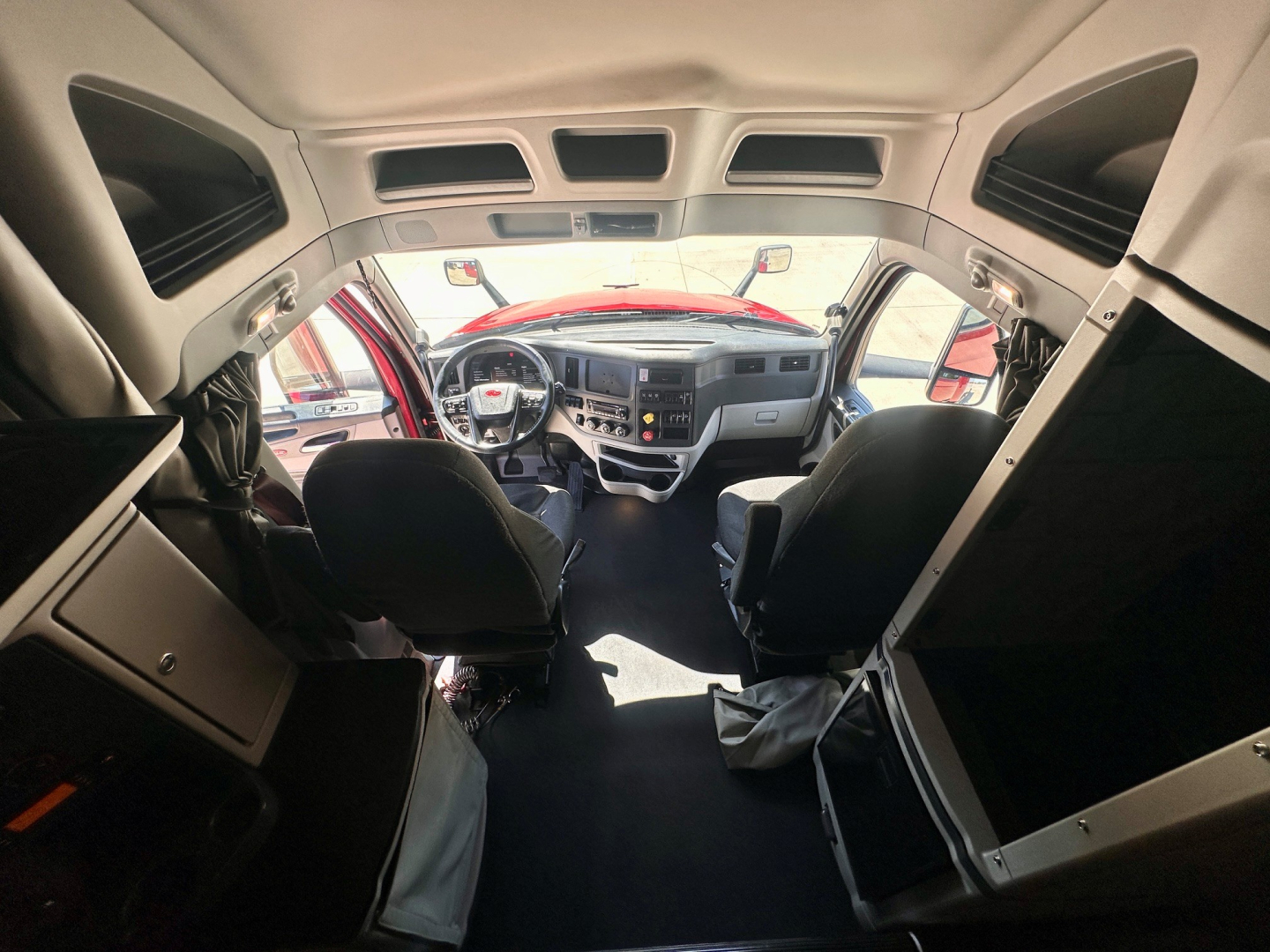 Peterbilt 579 cab interior view from rear passenger area showing dashboard, steering wheel, and driver seat in a sleeper truck.