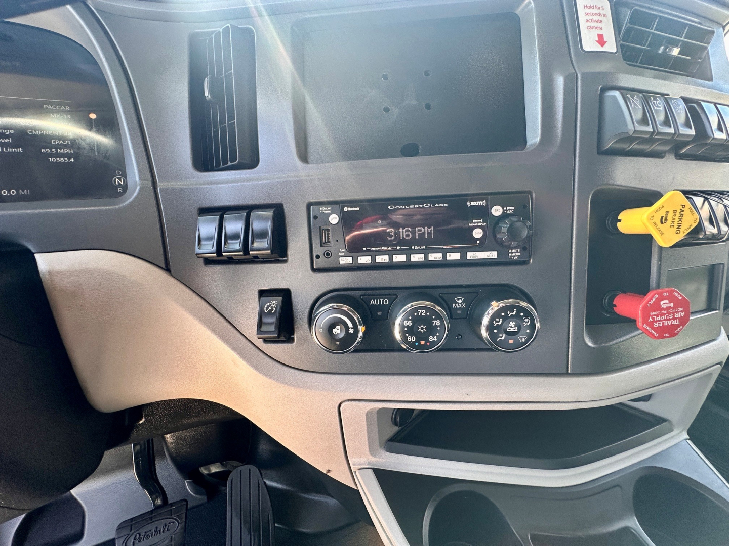 Peterbilt 579 dash area showing center console with radio, climate controls, and switches; yellow and red controls to the right; empty gauge cluster slot above; light gray dashboard.
