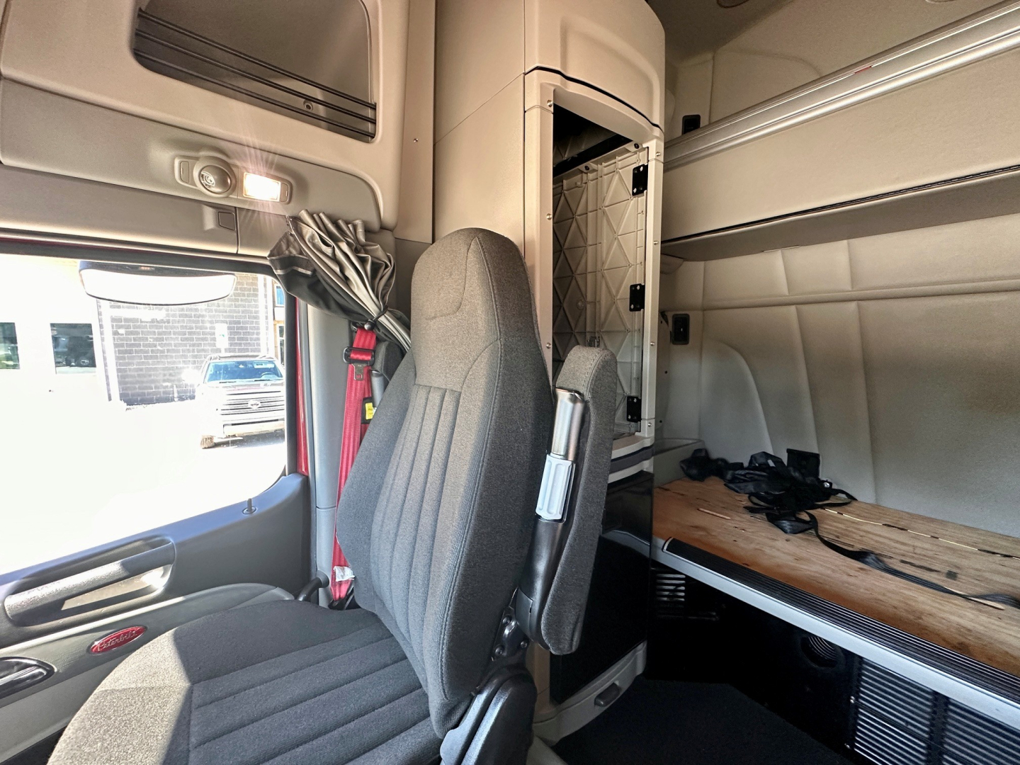 Peterbilt truck interior cab area with driver seat, sleeper area, and overhead storage; visible side window and dashboard edge.