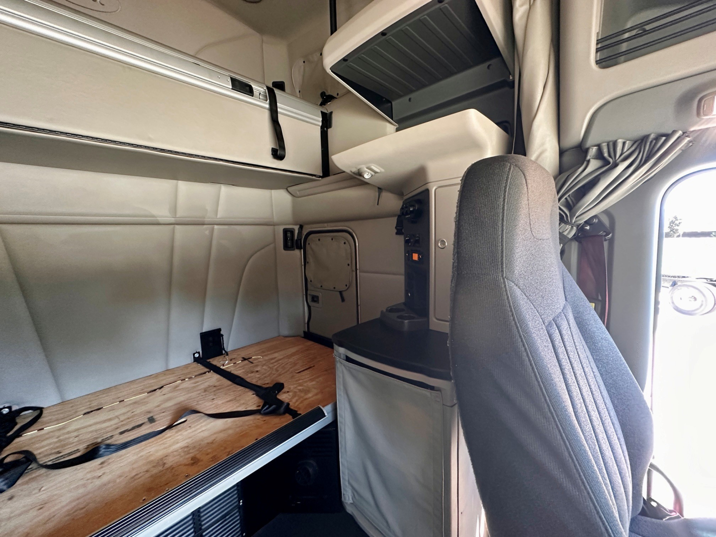 Peterbilt 579 cab interior showing sleeper area with wooden platform, overhead storage, and driver's seat; interior panels and a small cabinet visible.