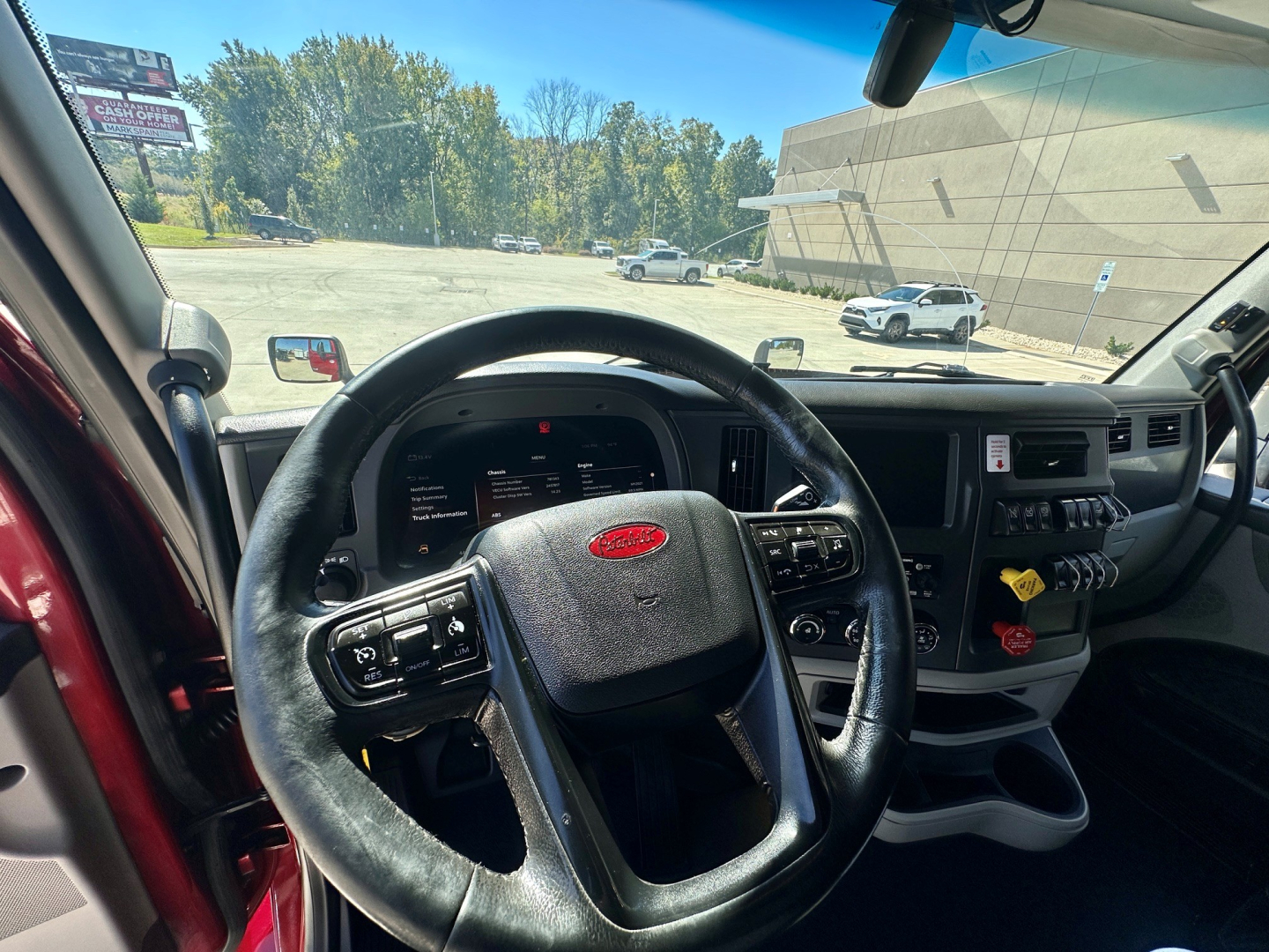Interior of a 2023 Peterbilt 579 cab showing steering wheel, dashboard, and center console. Visible Peterbilt emblem on steering wheel; various controls and panels on the dash.