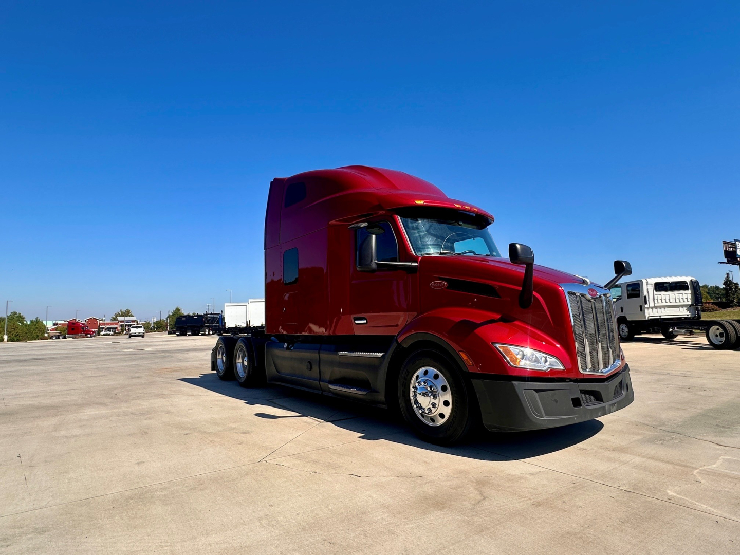 Peterbilt 579 truck in red paint, side view showing sleeper cab, chrome wheels, and long hood on a truck lot.