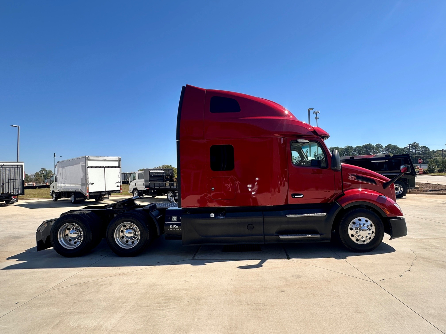 Side view of a red 2023 Peterbilt 579 conventional sleeper truck, showing cab and dual rear axles, with chrome wheels and black lower body panels.