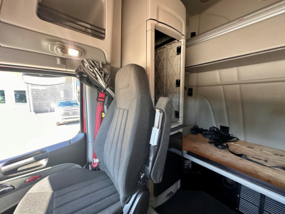 Peterbilt truck interior cab area with driver seat, sleeper area, and overhead storage; visible side window and dashboard edge.
