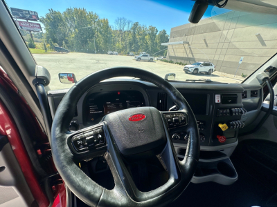 Interior of a 2023 Peterbilt 579 cab showing steering wheel, dashboard, and center console. Visible Peterbilt emblem on steering wheel; various controls and panels on the dash.